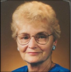 Portrait of an older white woman with short blonde hair, glasses and an enigmatic smile